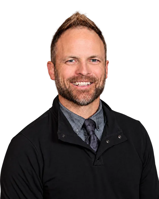 Brady Baxter, smiling, wearing a black pullover over a shirt and tie